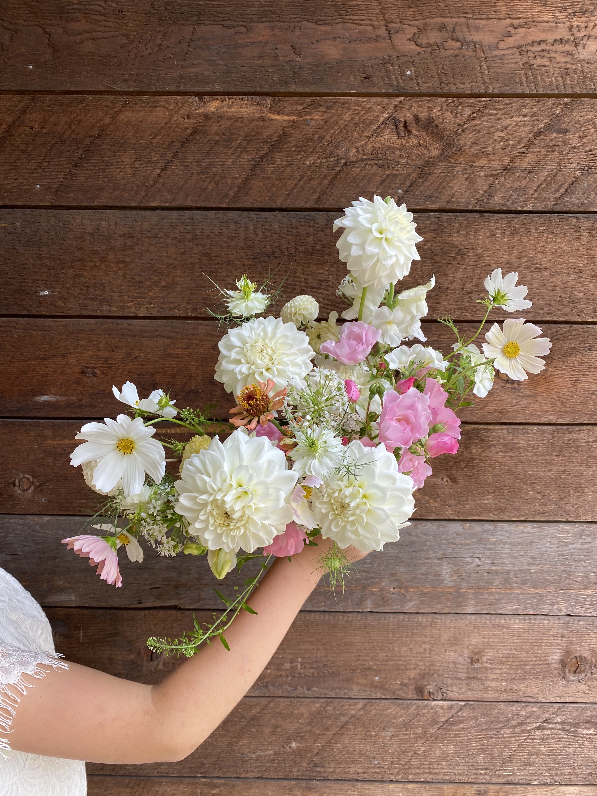 Person holding a bridal bouquet of white and pink flowers against a wooden background.