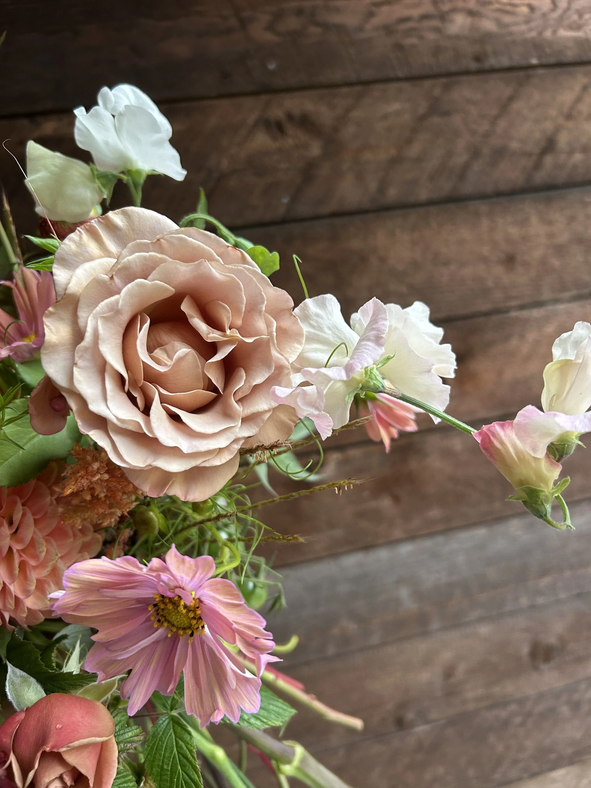 Close-up of a bouquet with light pink, white, and peach flowers against a wooden background.