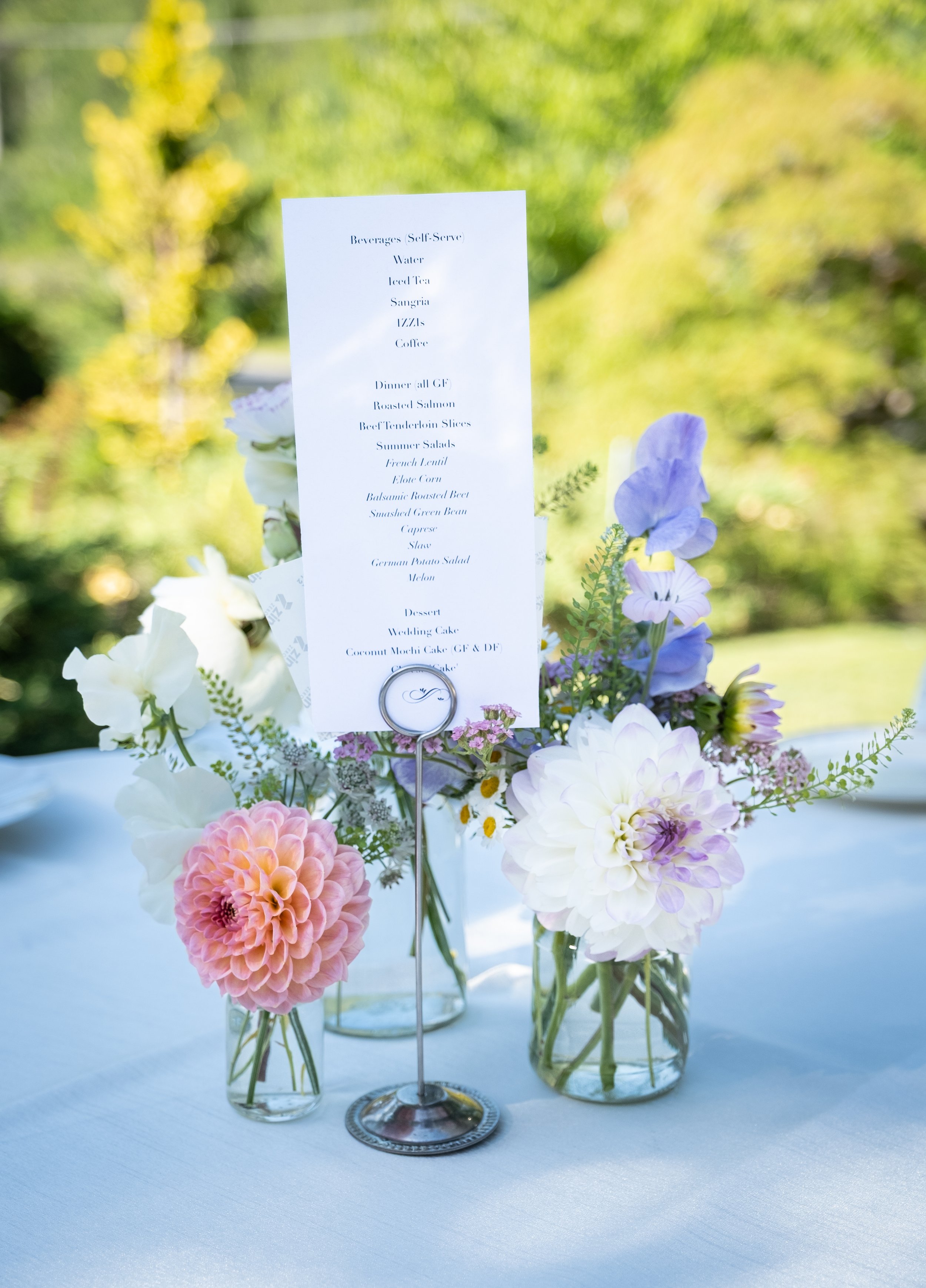 Wedding reception table with a floral centerpiece featuring pink, white, purple, and blue flowers, and a printed menu card standing in a holder.
