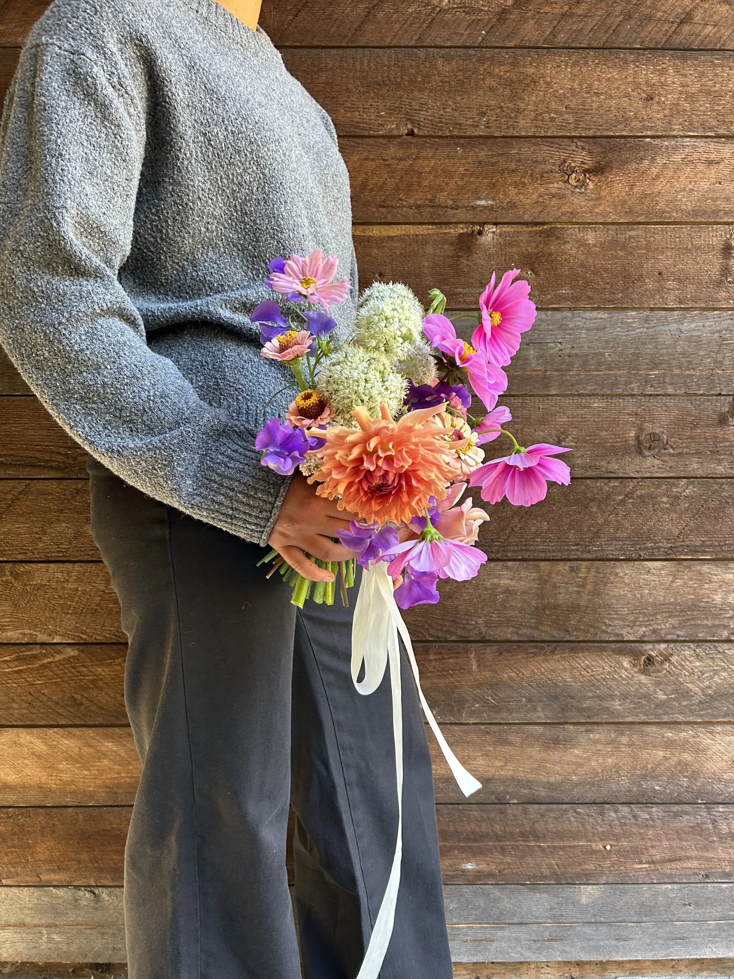 Person holding a bridal bouquet of colorful flowers against a wooden background.