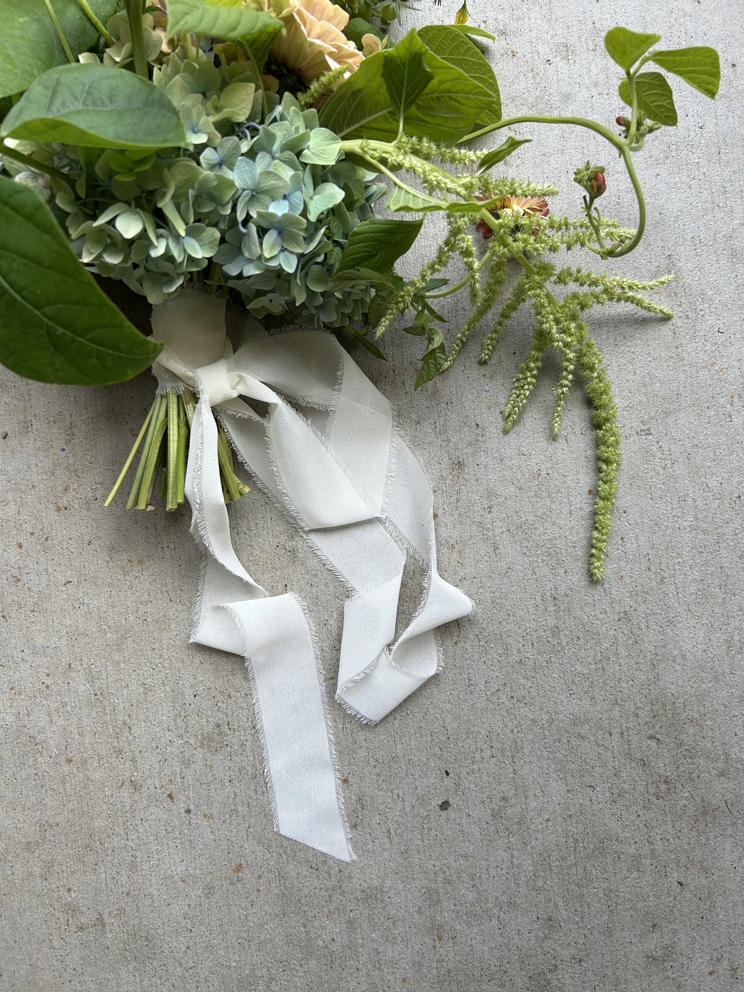 Bouquet of green leaves and flowers tied with a white ribbon on a concrete surface.