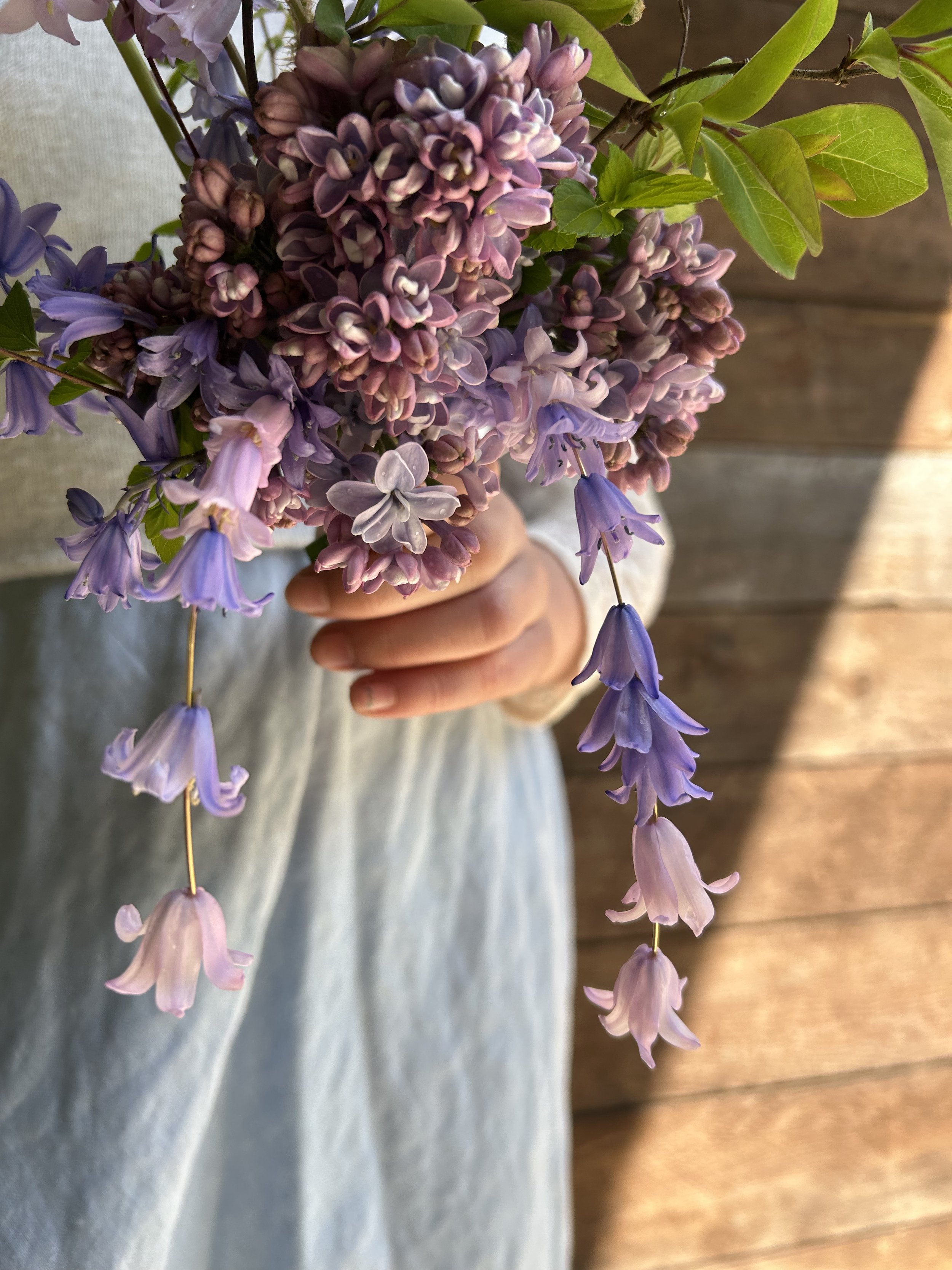 Person holding a bouquet of purple and pink hyacinth flowers with a wooden wall background.