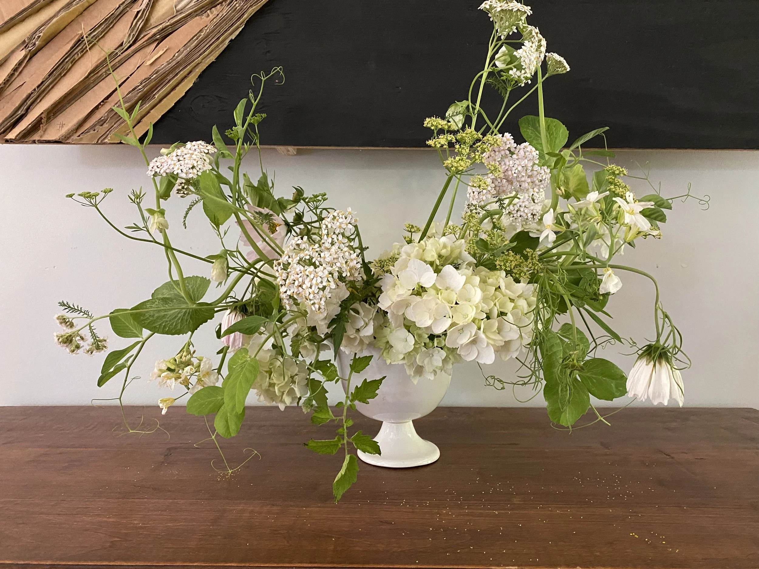 White floral arrangement in a white vase on a wooden table.