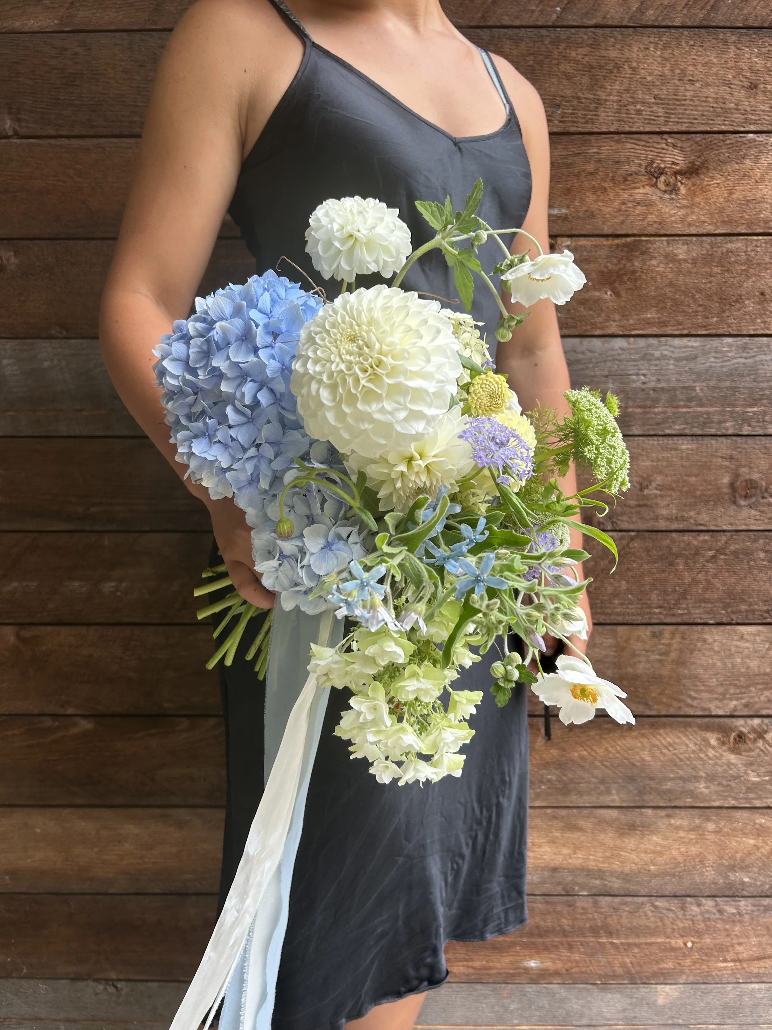 A woman holding a bouquet of white, blue, and purple flowers against a wooden background.
