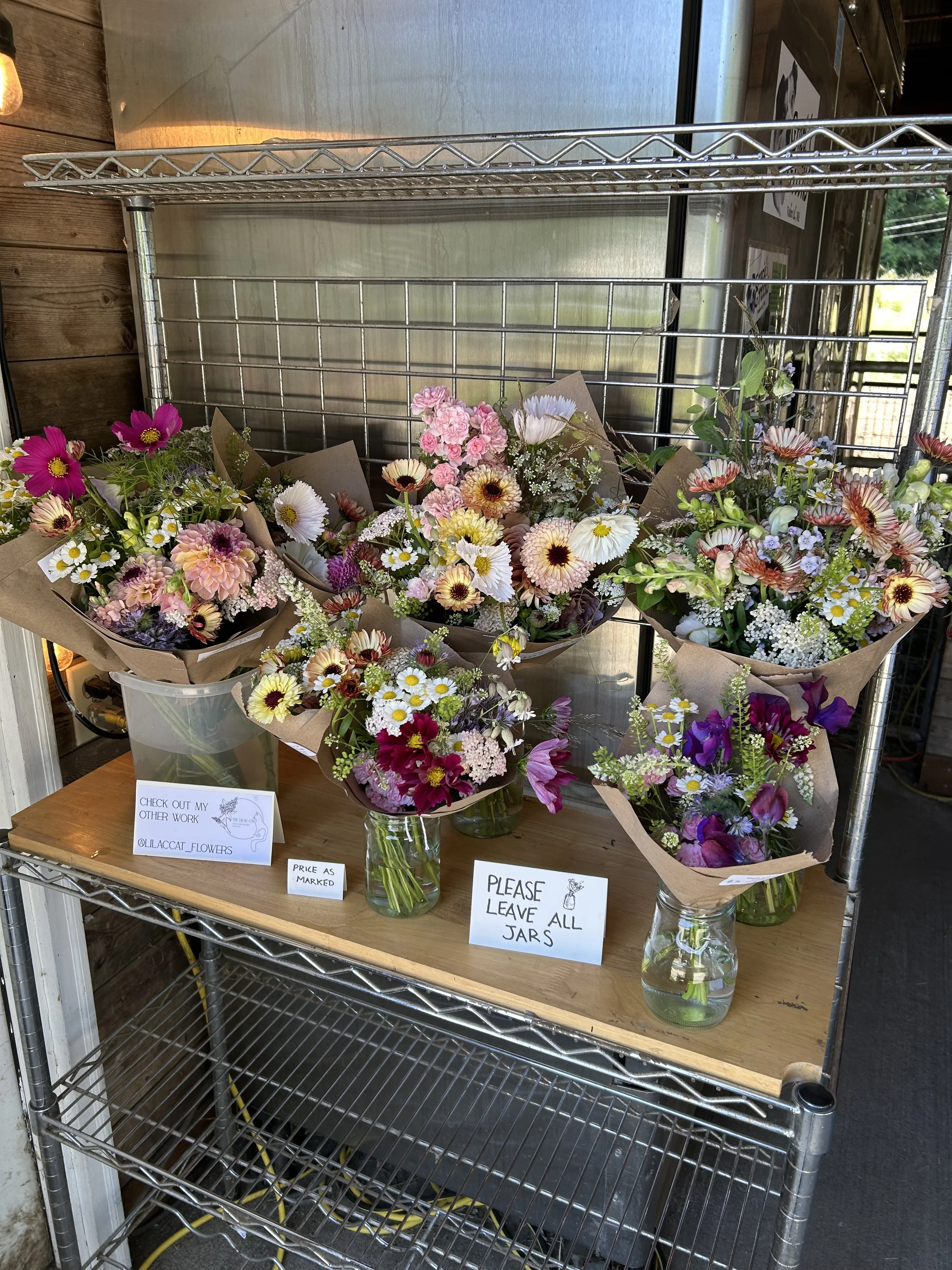 Display of various flower bouquets in glass jars on a metal shelving unit at a flower shop.