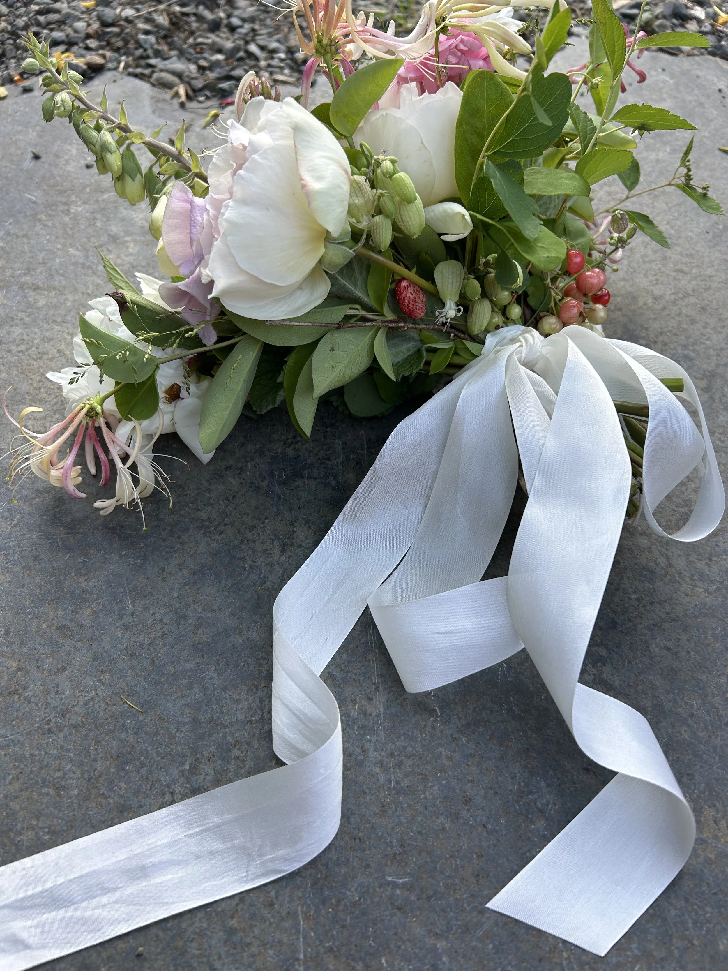 A bouquet of white, pink, and green flowers with a white ribbon on a gray stone surface.