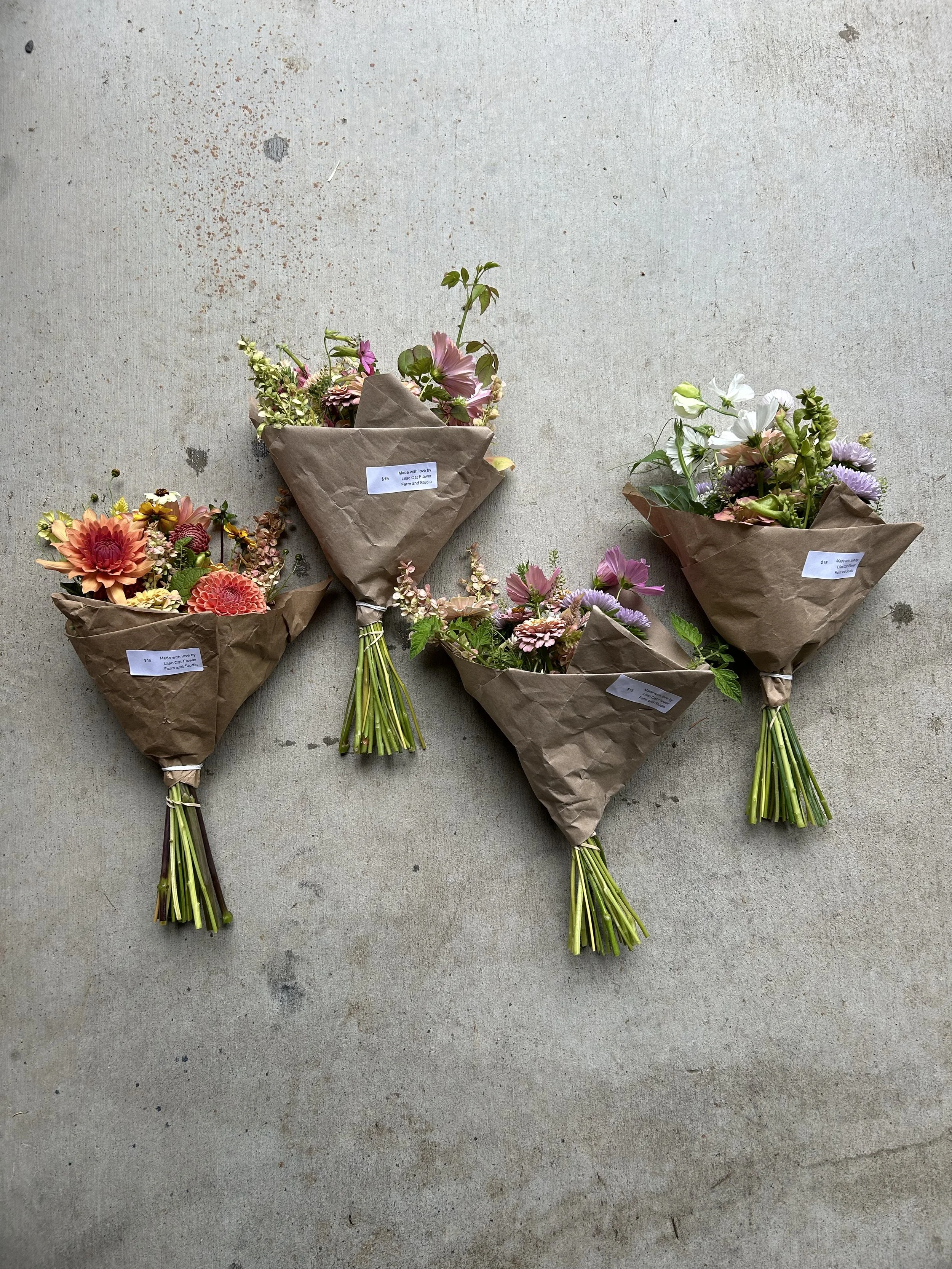 Four bouquets of flowers wrapped in brown craft paper, laid on a concrete surface.