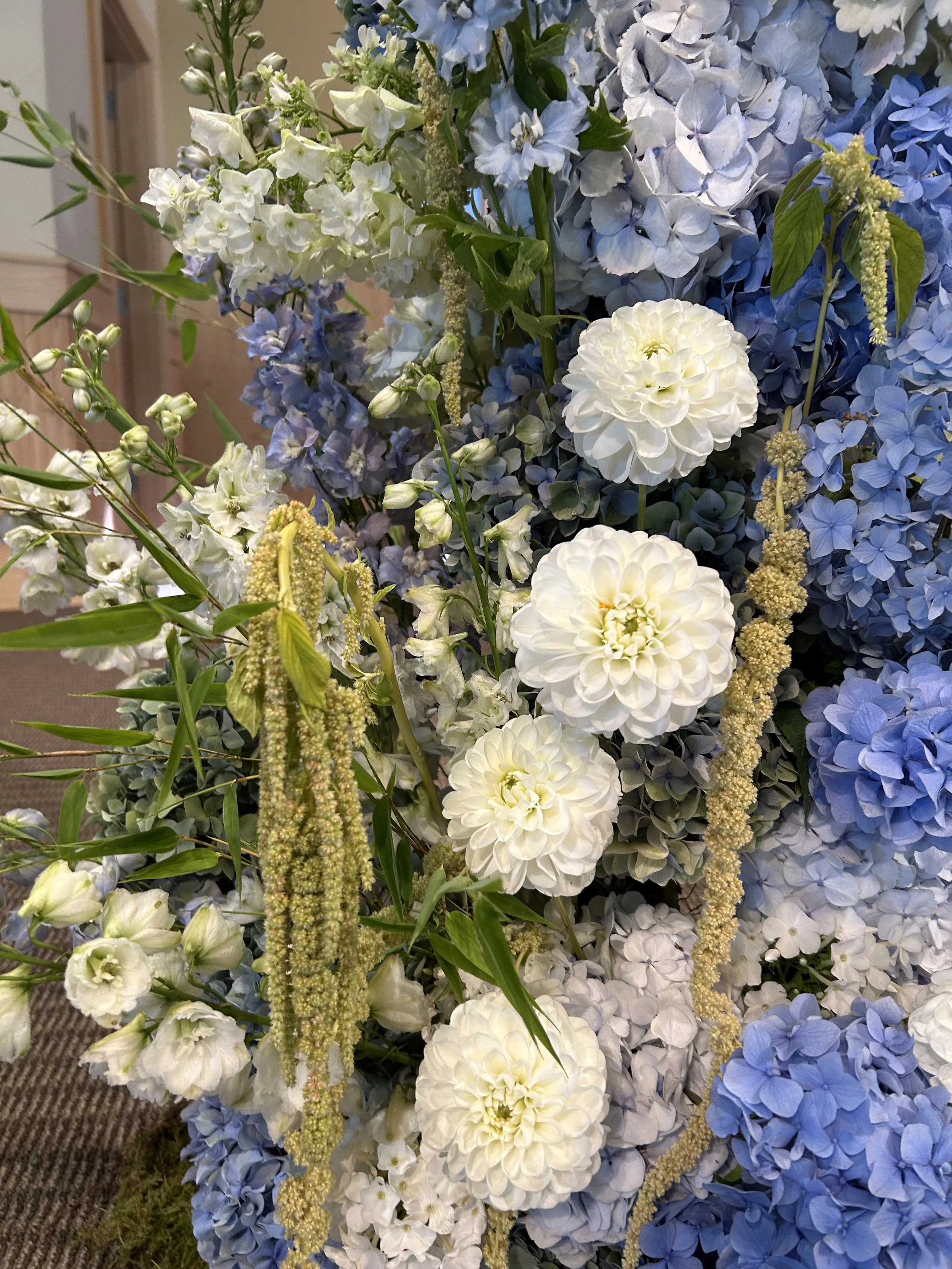 A bouquet of white and light blue hydrangeas with white dahlias and green foliage.