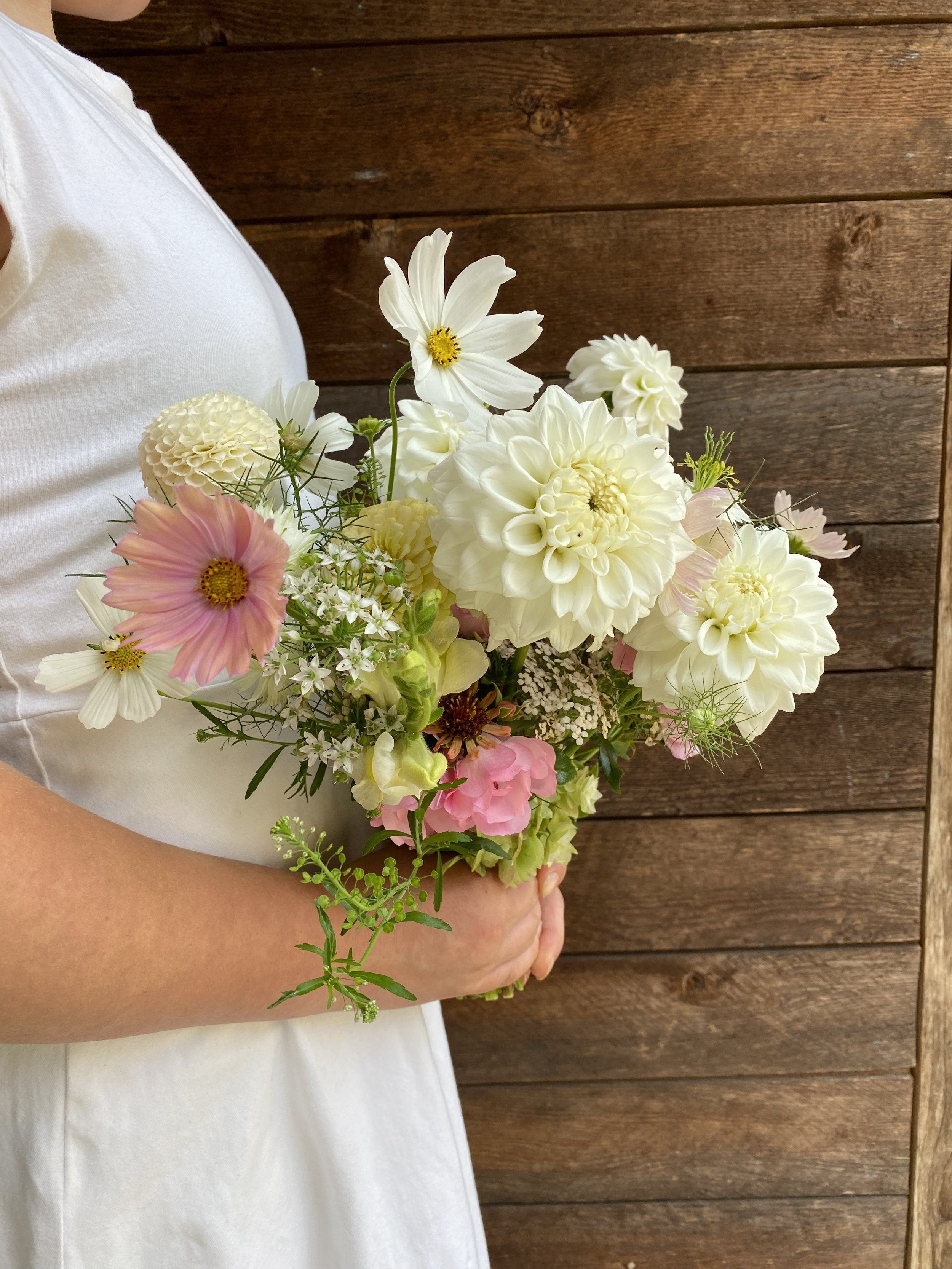 Person holding a bridal bouquet of white and pink flowers against a wooden wall background.