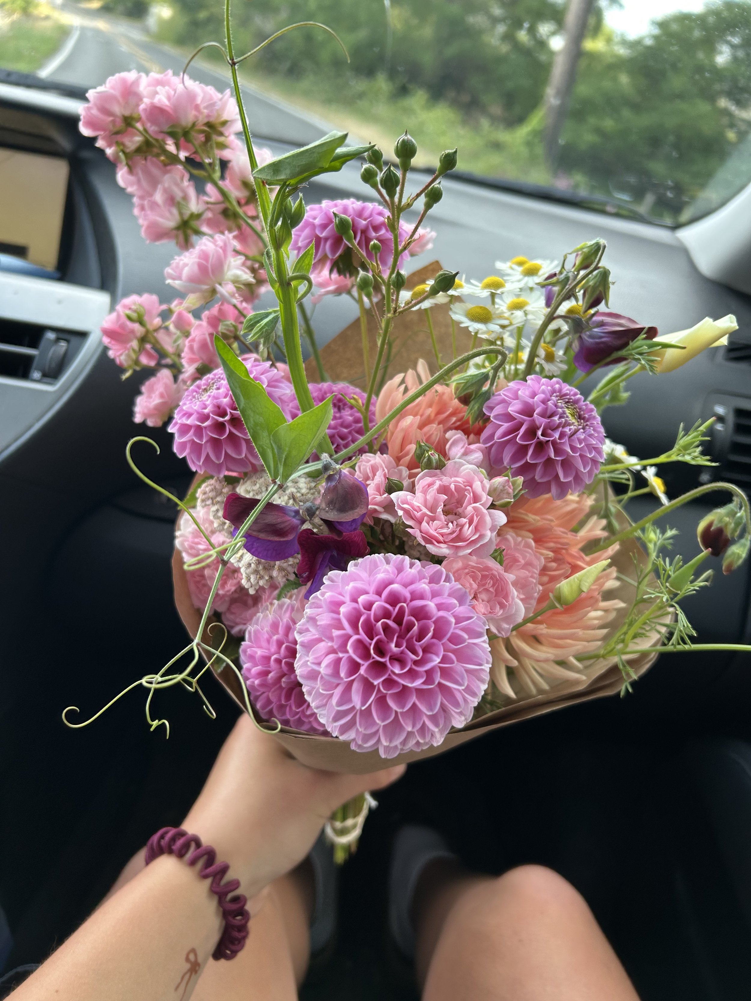 A person holding a bouquet of pink, purple, white, and yellow flowers inside a car.