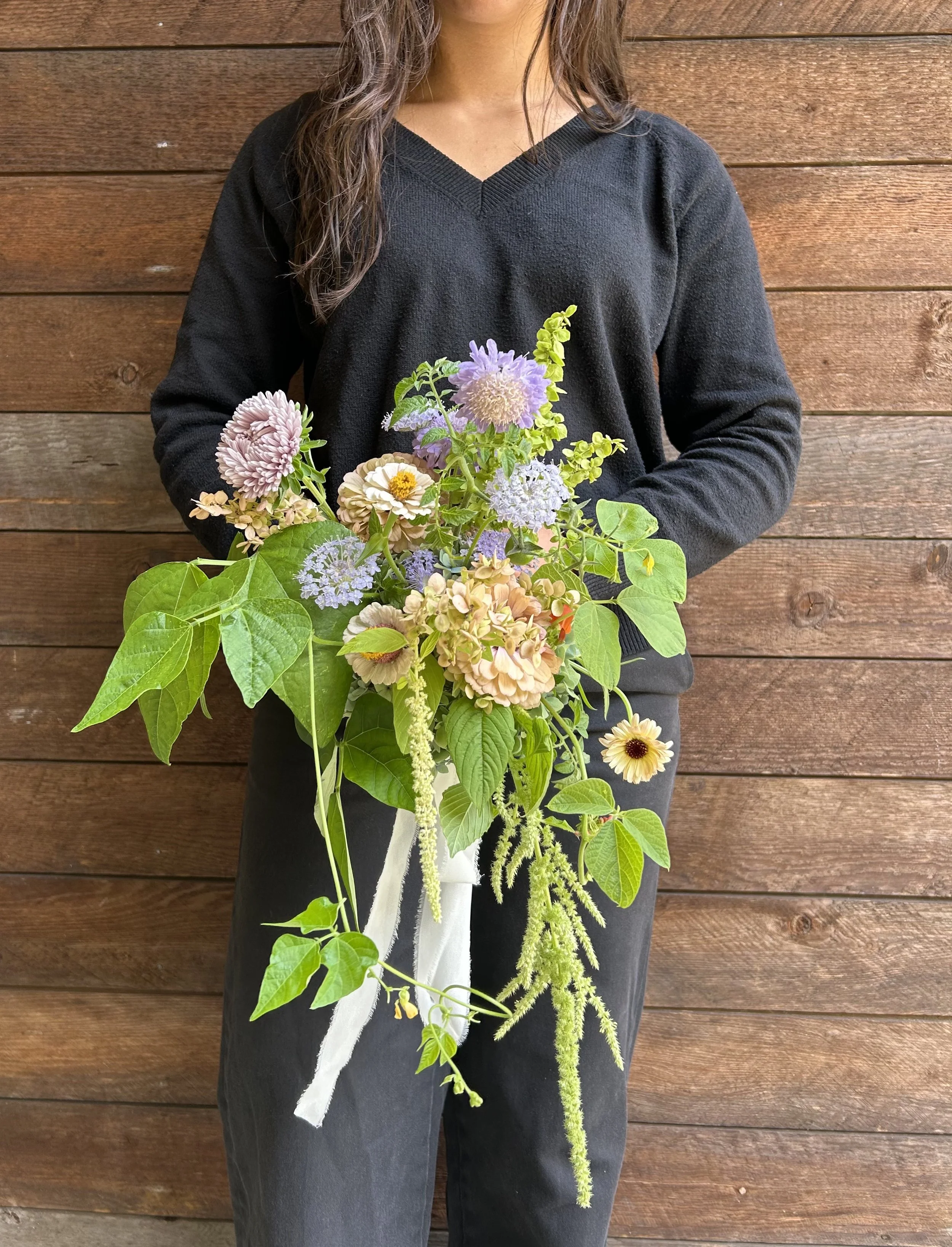 Person holding a textural bridal bouquet of flowers in front of a wooden wall.