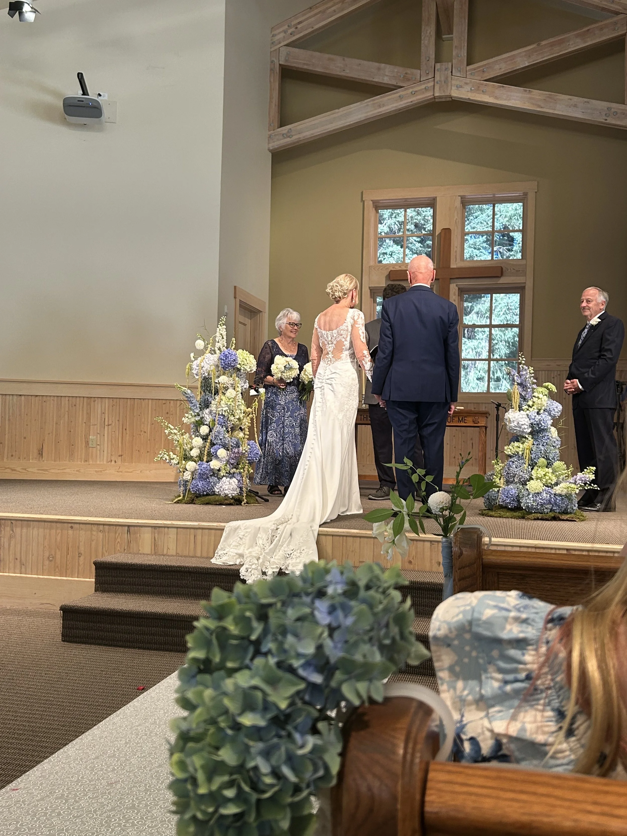 Bride and groom exchanging vows at a wedding ceremony inside a church with family members and floral arrangements.