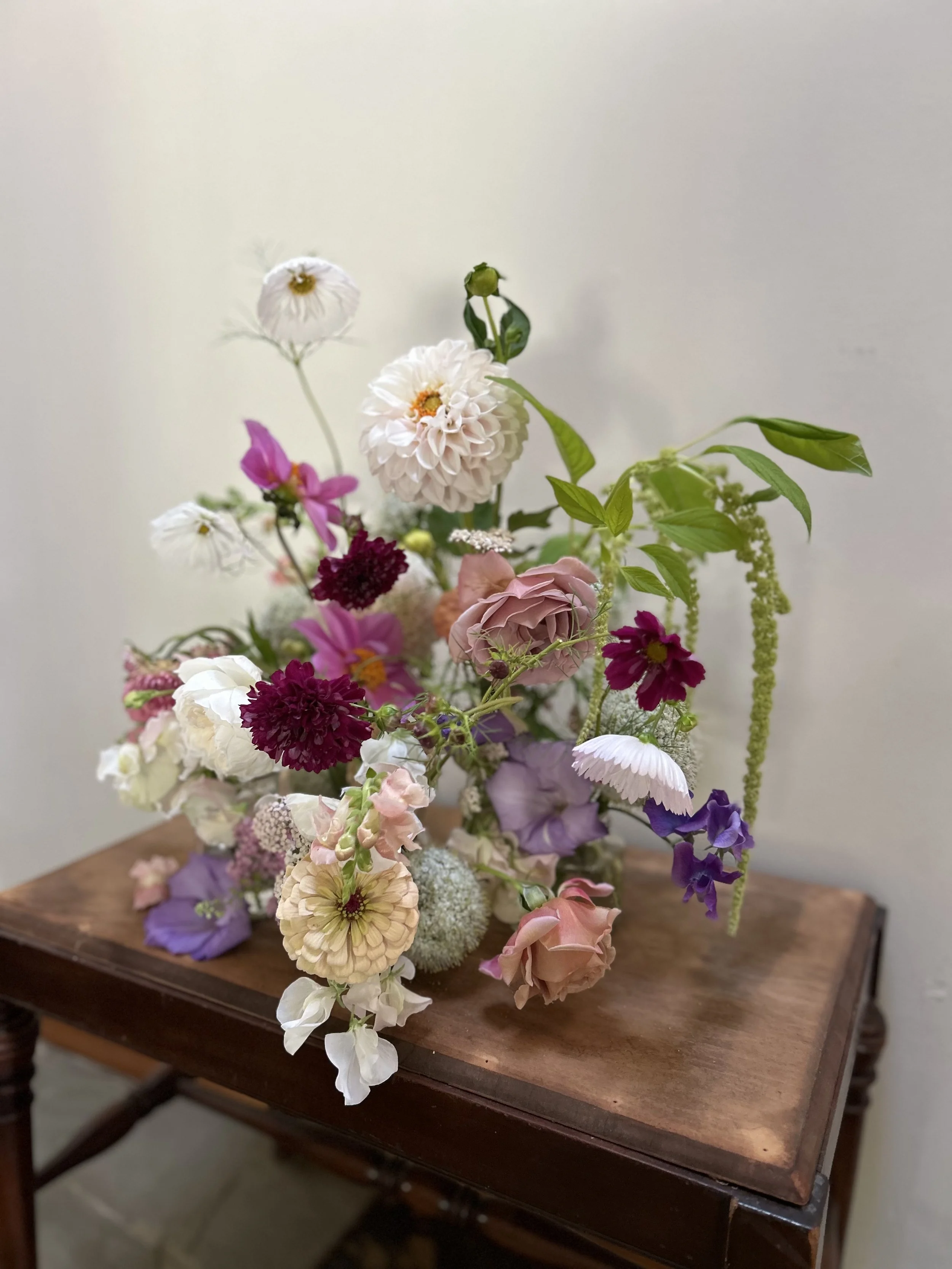 A colorful bouquet of various flowers arranged on a wooden table against a plain wall.