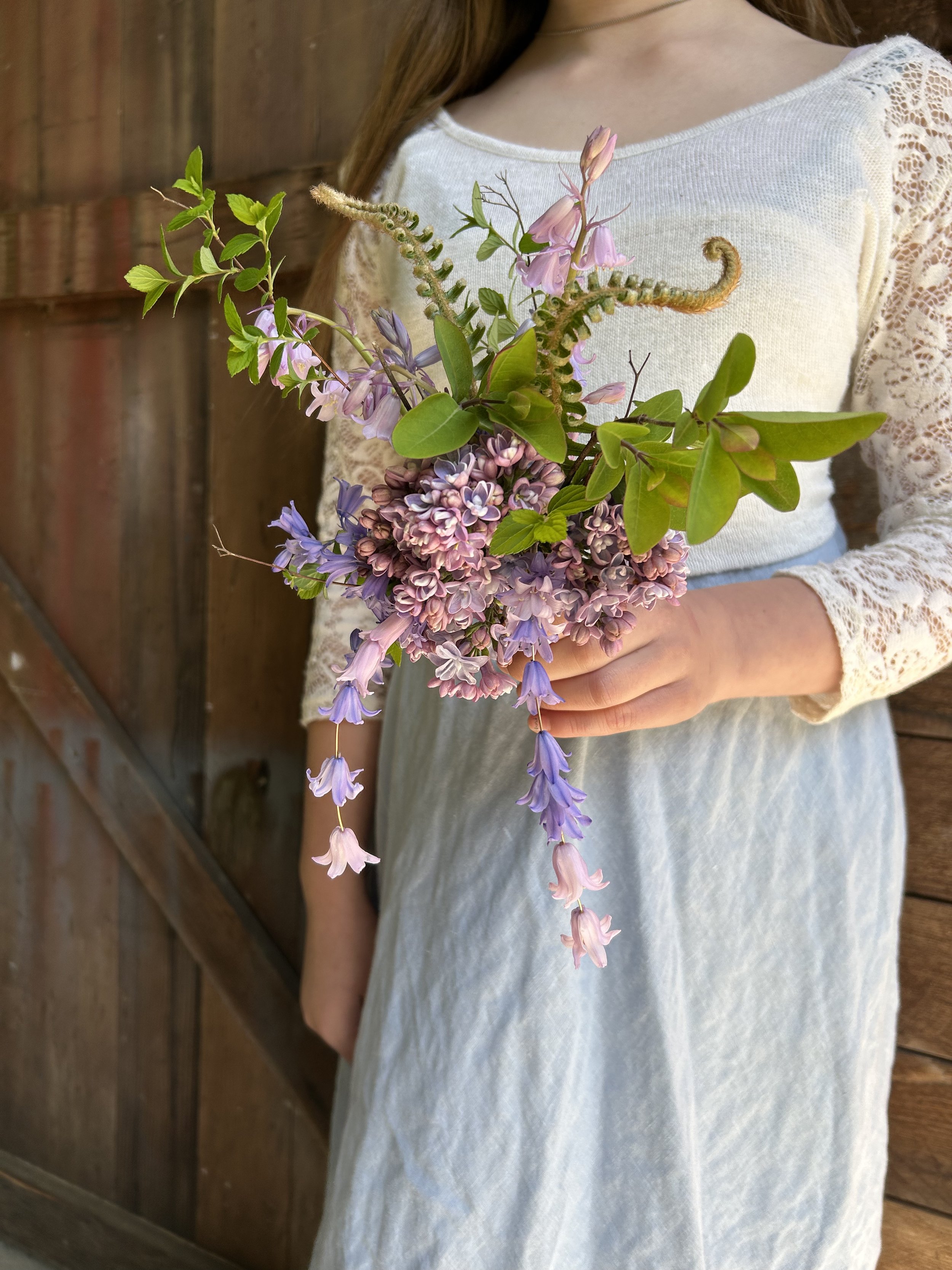 Woman holding a bouquet of purple and pink flowers in front of a wooden fence.
