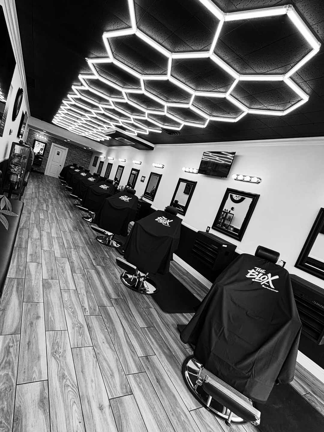 Photo of the interior of the barber shop. Row of barber chairs with barber capes that say "The BLOX". Clean and presentable to showcase the barbershop.