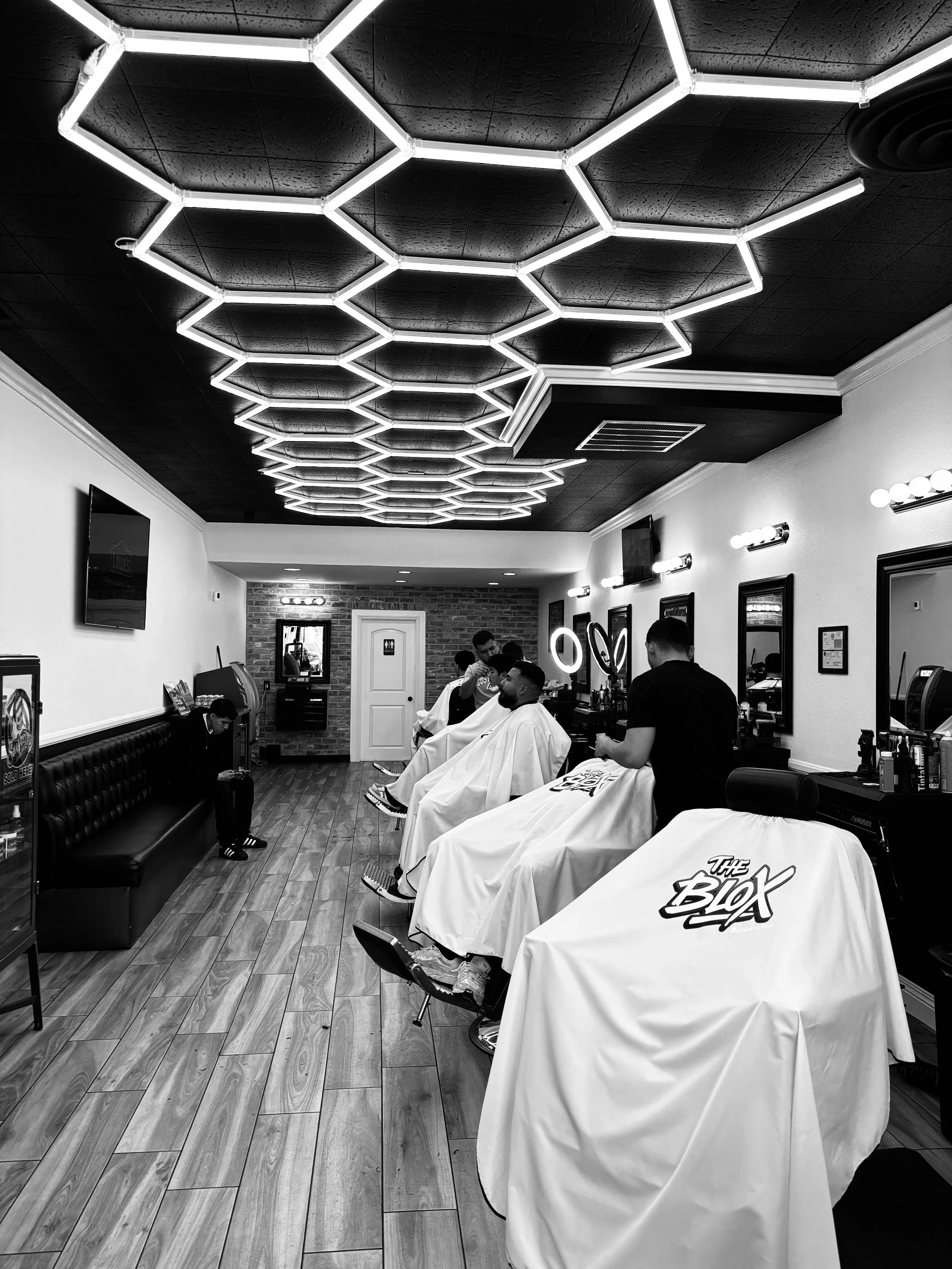 Row of seats with clients on barber's chair getting a haircut inside of the barbershop.