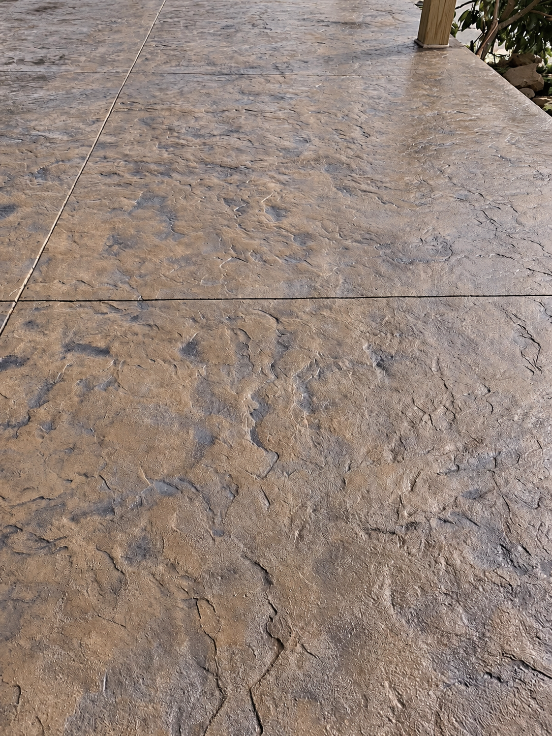 Close-up view of a textured concrete or stone surface with visible cracks, in a neutral brown color.