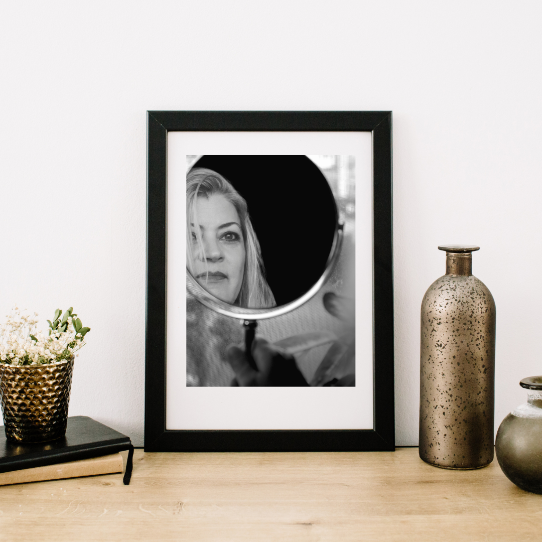 A black and white portrait of a model looking into a mirror