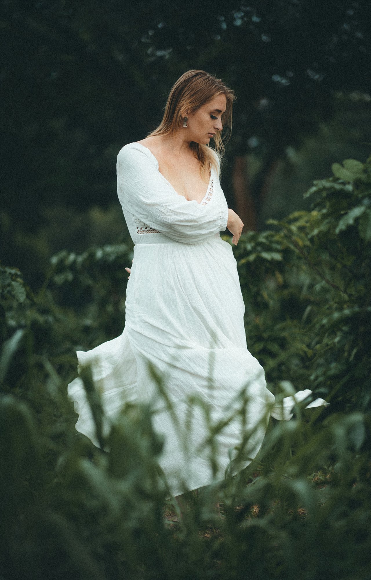Mujer con vestido blanco en un entorno natural con vegetación densa.