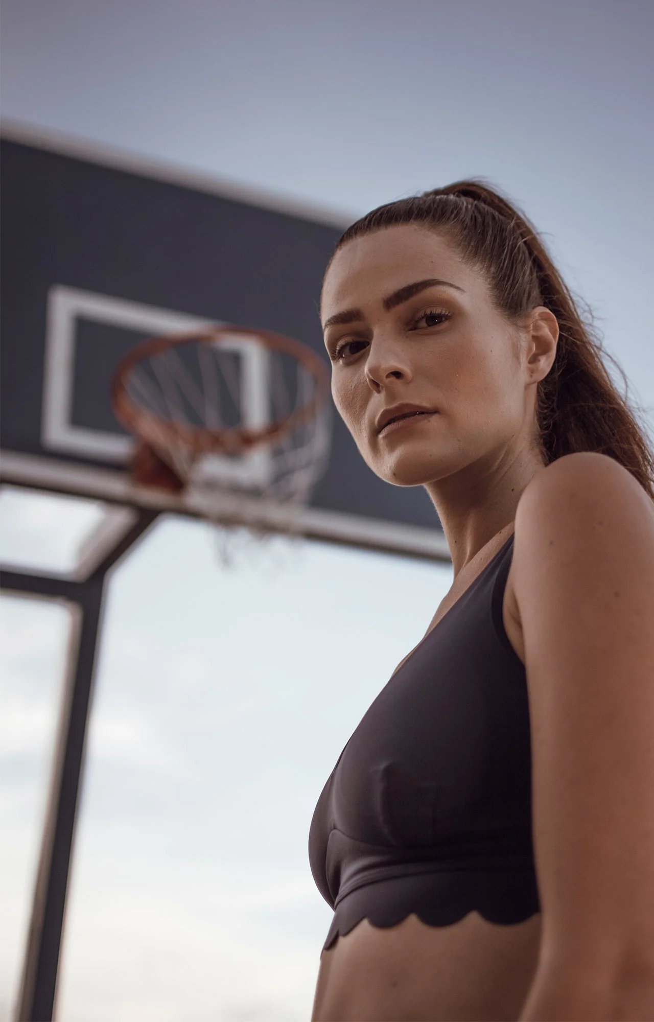 Mujer con expresión de confianza en un gimnasio, vista de medio cuerpo con fondo de armazón de baloncesto.