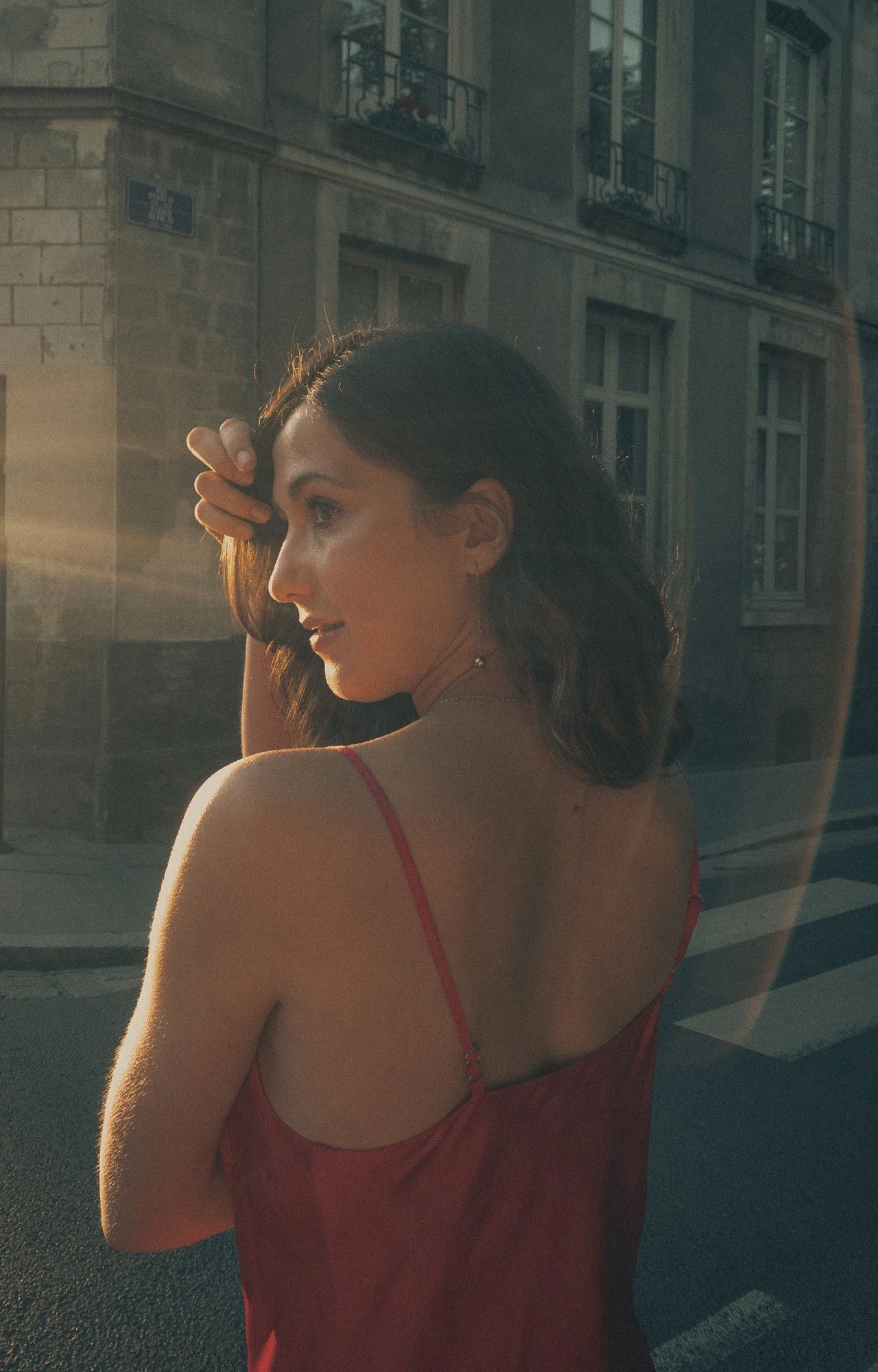 Mujer con vestido rojo mirando por la ventana en una calle urbana durante el atardecer.