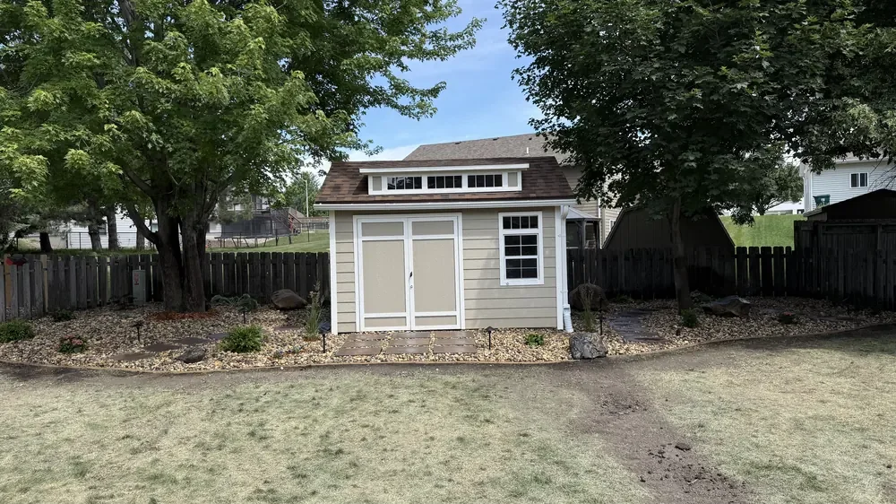 Backyard shed framed by a rock bed with stepping stone path and ornamental grasses, daytime