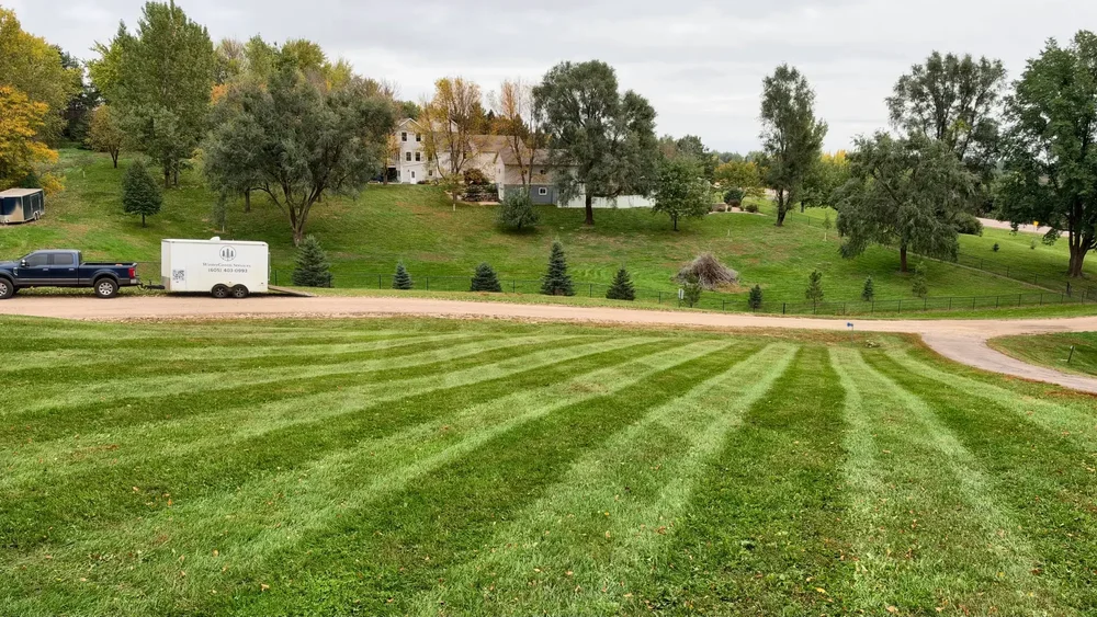Freshly striped acreage lawn with the WinterGreen Services truck and trailer parked along the road