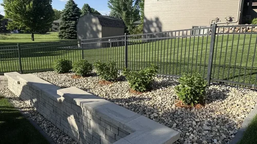 Corner detail of a gray block retaining wall with rock bed and small evergreen shrubs