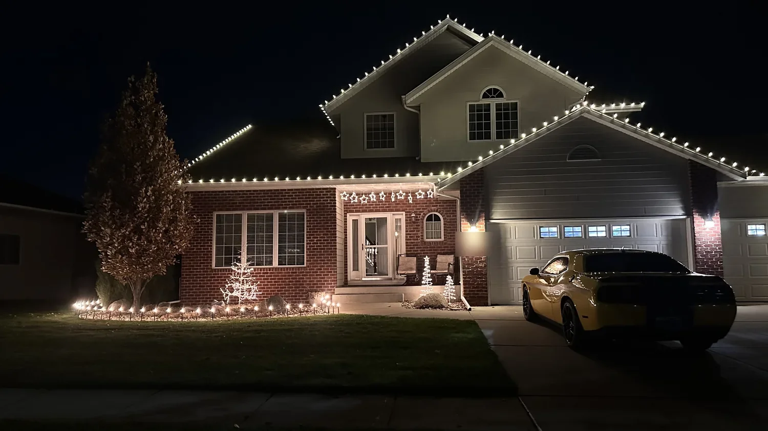 Two-story brick home in Sioux Falls, SD with white C9 roofline lights, lit spiral trees, and star lights over the entry