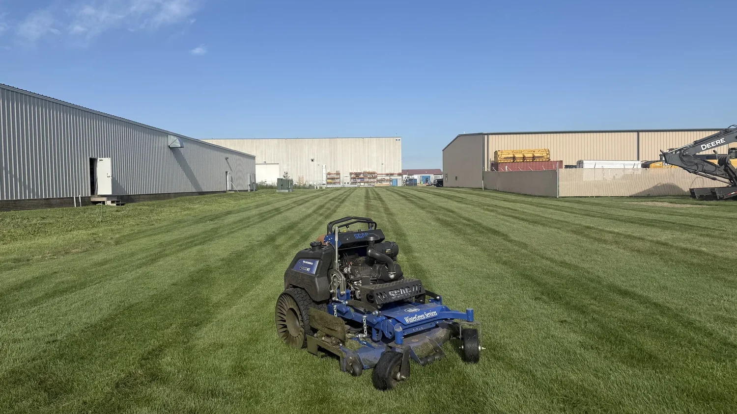 Mower on a large striped commercial lawn between two warehouse buildings