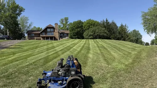 Wide striped lawn on a sloped acreage property with a cedar home at the top of the hill