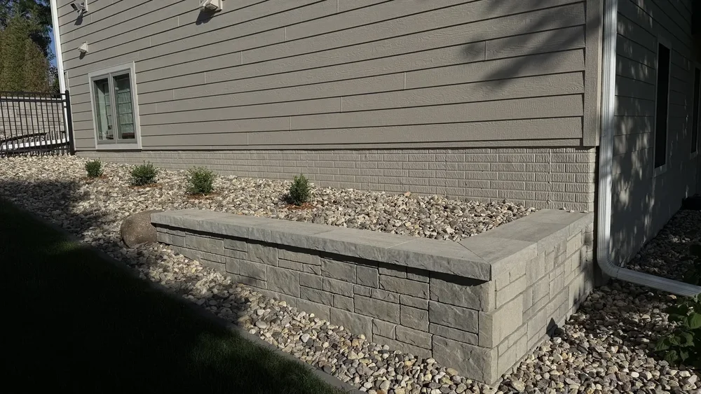 Block retaining wall with capstone edging enclosing a rock bed of newly planted shrubs