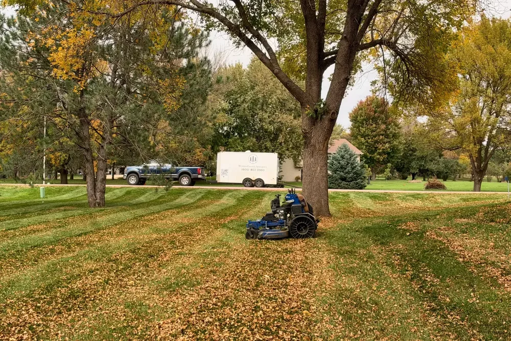 WinterGreen Services truck and enclosed trailer parked at a customer's property, with a stand-on mower on the lawn