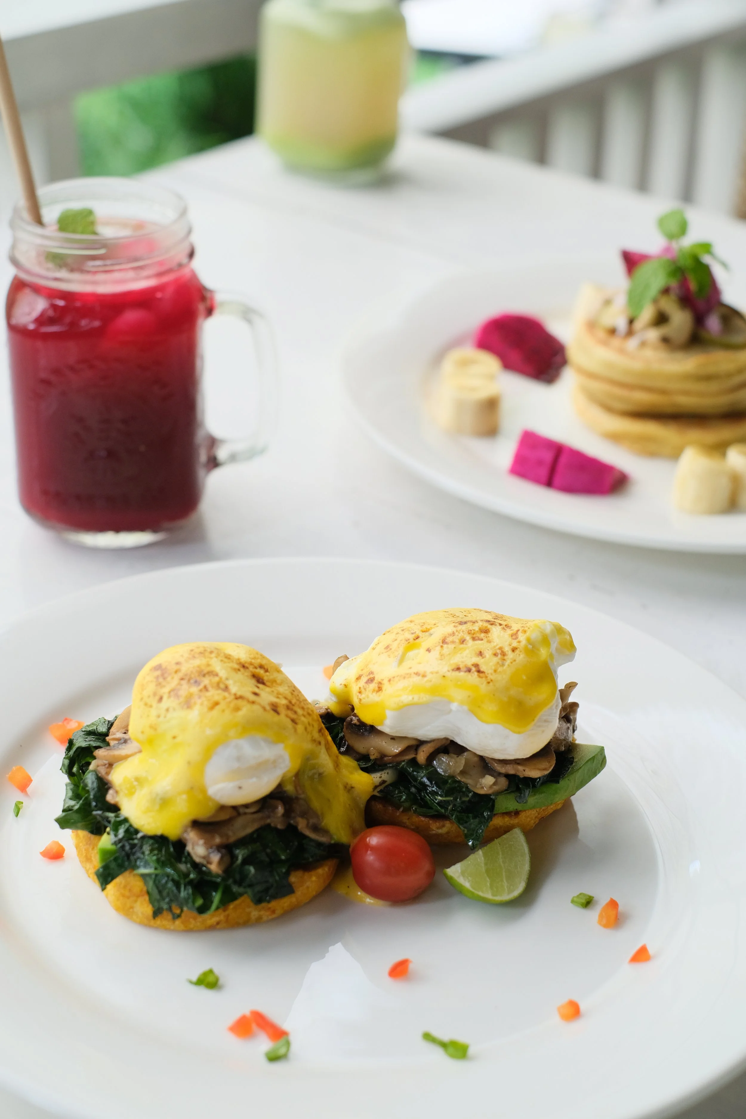 Two eggs Benedict on an English muffin with spinach and mushrooms, garnished with a cherry tomato and lime wedge at Unity Cafe Bali