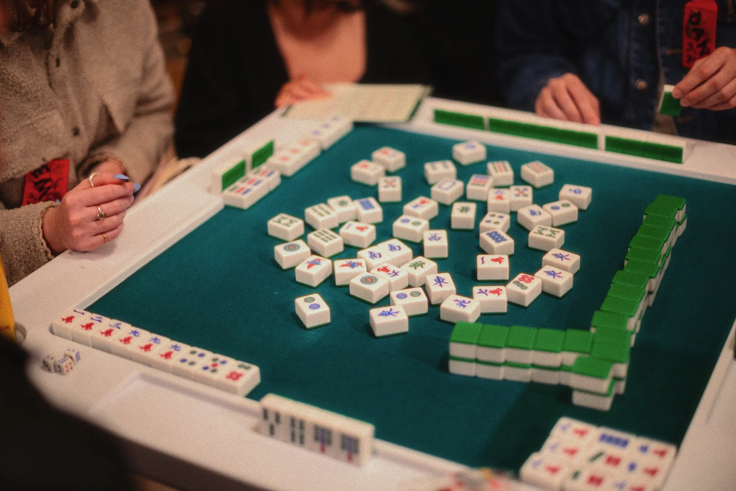 People playing a game of Mahjong with a green felt table and various tiles spread out