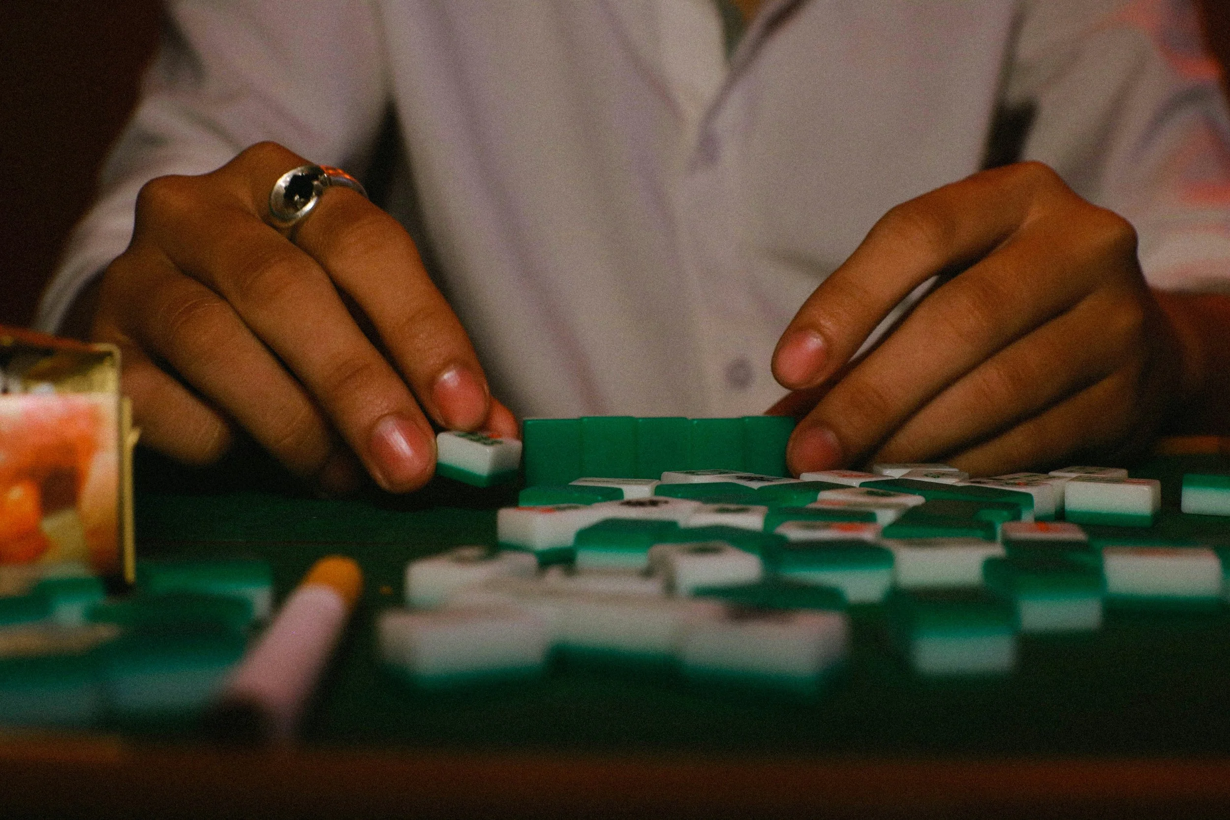 Person playing dominoes at a table with a dark background, focusing on their hands and the domino pieces.