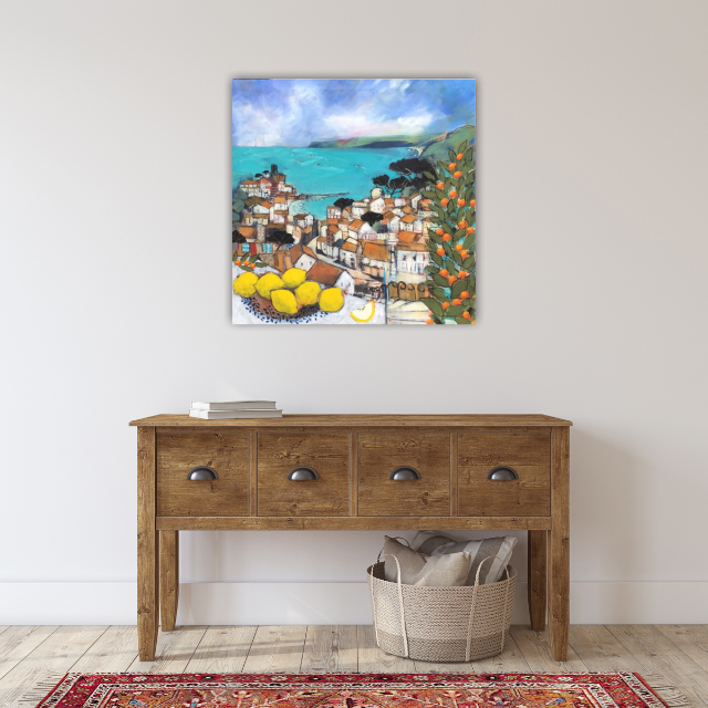 Colorful landscape painting of a coastal village with houses, trees, and a body of water, hanging above a wooden console table in a minimalist interior.