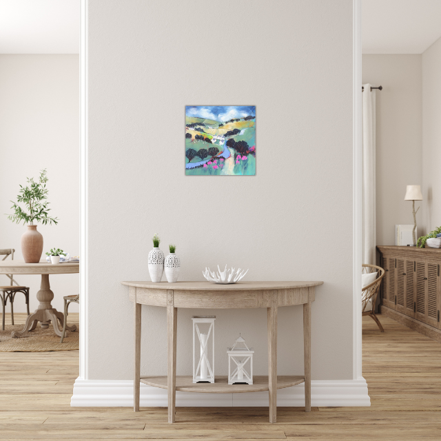 A small wooden console table against a light-colored wall with a colorful landscape painting above, two white vases with small plants, and decorative lanterns on the floor.