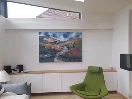 Interior of a modern living room with a large landscape painting on the wall, a green lounge chair, a white sideboard, and a flat-screen TV mounted on the wall.