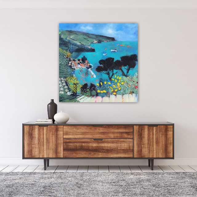 Abstract landscape painting of a coastal scene with hills, trees, and boats on the water, hanging above a modern wooden console with sculptures and books.