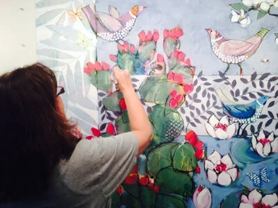Person painting a colorful mural featuring birds and flowers on a wall.