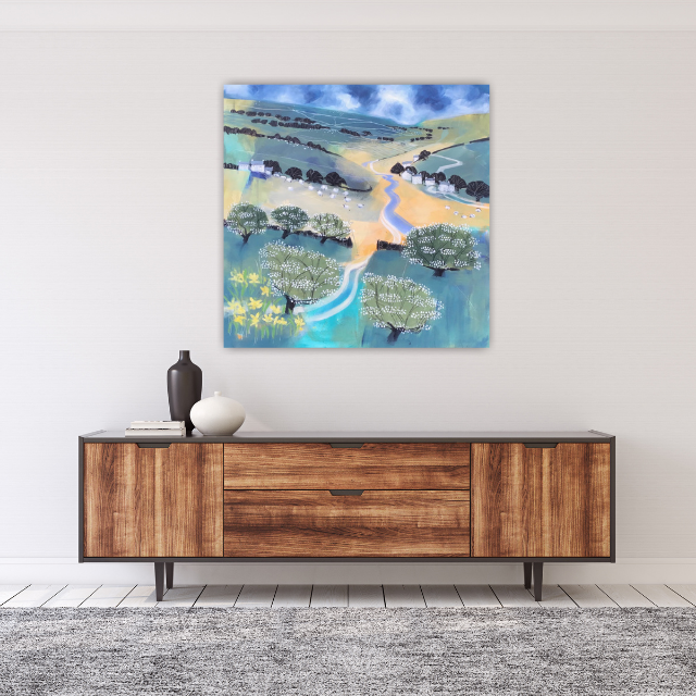 Abstract landscape painting of rolling green hills, stylized trees, a winding river, and a partly cloudy sky, hung above a wooden sideboard with decorative vases.