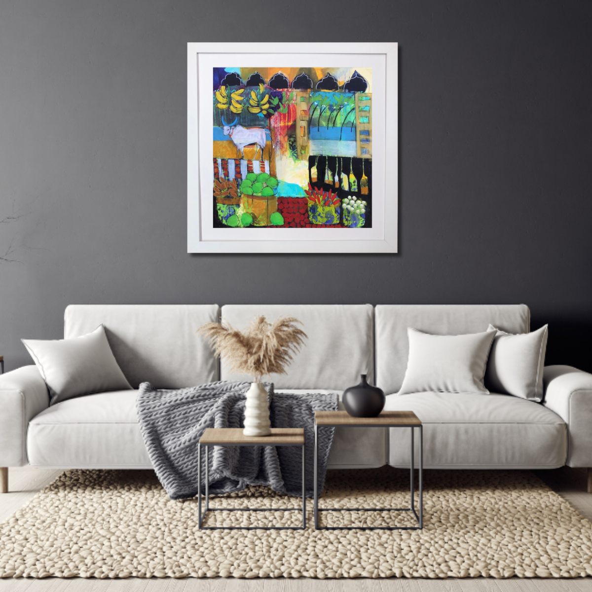 Colorful abstract painting of a farm scene with a goat, bananas, vegetables, and greenery hanging on a dark gray wall above a white sofa with pillows, a blanket, and a coffee table with vases in a modern living room.