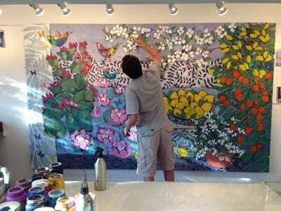 Person painting a colorful mural with flowers, butterflies, and trees on a wall.