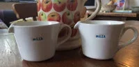 Two white coffee mugs on a wooden table with a blurred background.