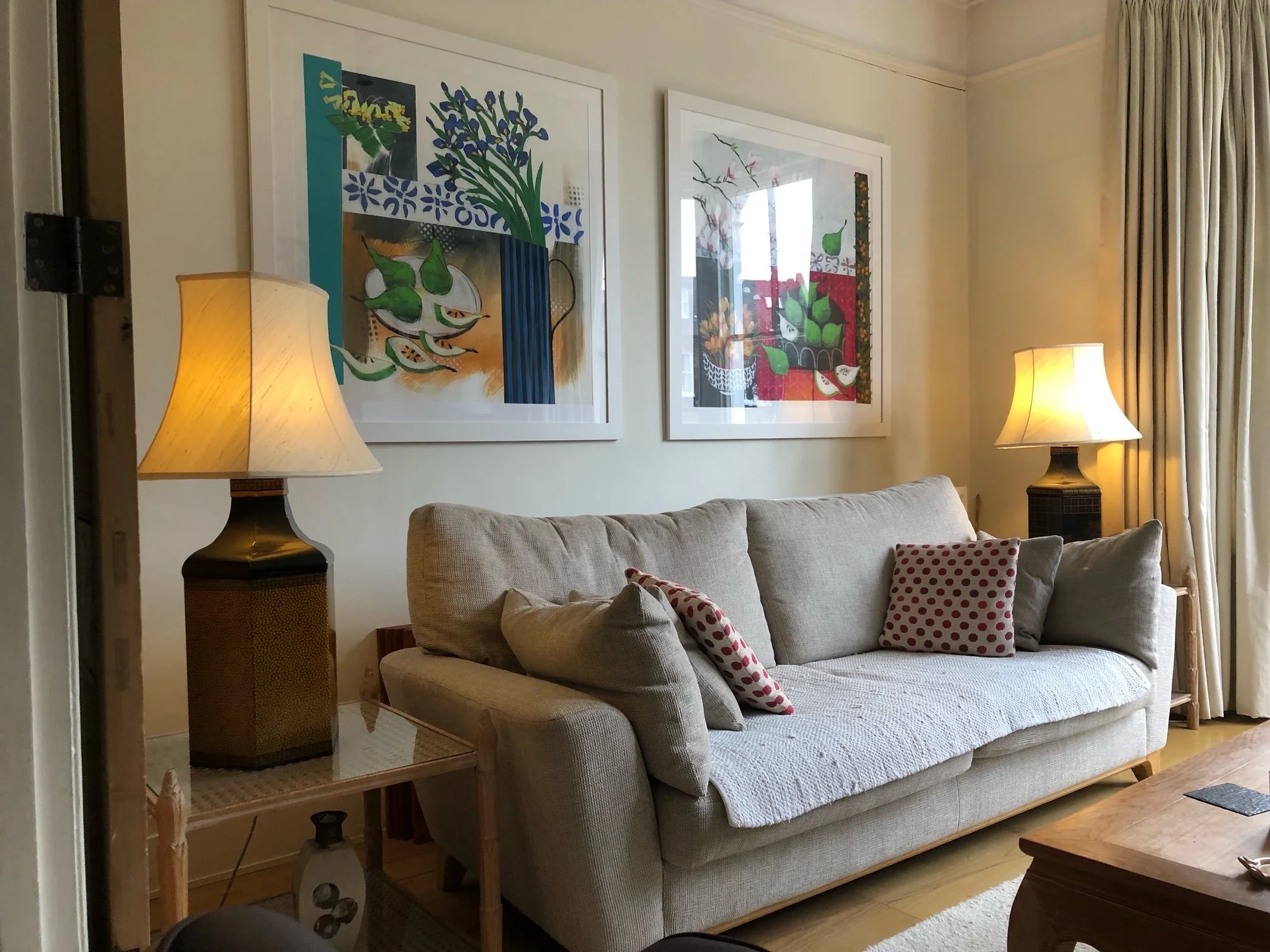 Living room with beige sofa decorated with polka dot pillows, two table lamps on either side, and colorful framed abstract art on the wall.