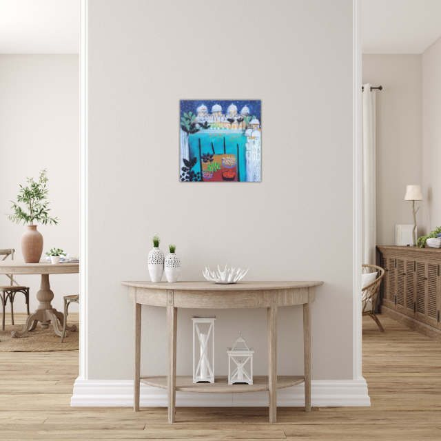 Colorful painting of a snowy mountain landscape hung on a white wall above a small wooden console table with decorative vases, a shell-shaped decor, and lanterns in a bright, minimalist living space.