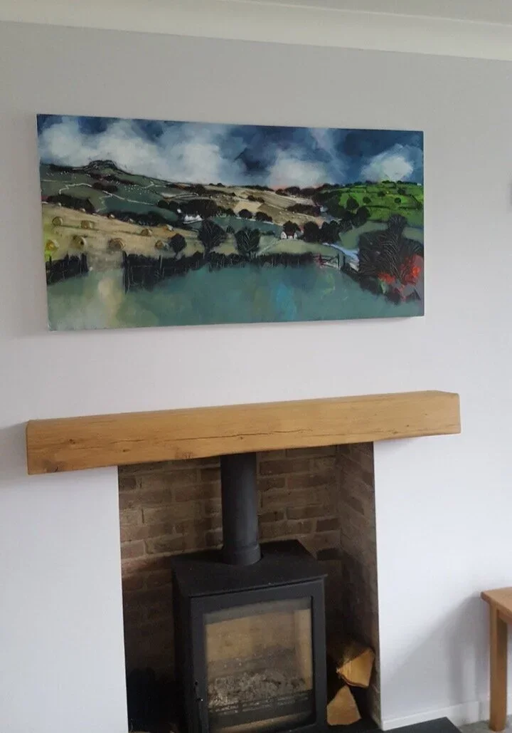 Painting of a countryside landscape hanging above a wood-burning stove in a room.