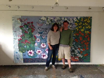 A woman and a man standing in front of a large colorful floral mural on a wall.