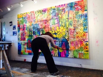 Person painting a colorful, abstract mural on a large wall in an art studio.